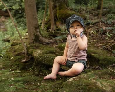 baby in baby bonnet sitting on mossy rocks