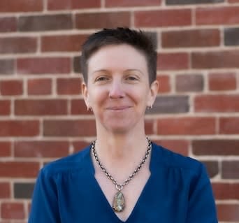 Caroline Malloy in a blue shirt in front of a red brick wall