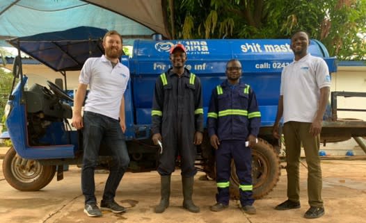 Four men standing in front of a small exhauster vehicle for pit latrine waste.