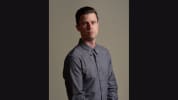 Dan Hoyle in a grey button up looking serious