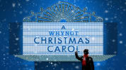 A Whynot Christmas Carol show art, featuring a Scrooge-looking man on a ladder fixing a marquee with the title