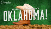 Cowboy boots and hat sit on a hay bale with a green background. Large white letters over the front say "Oklahoma!"