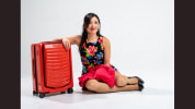 a woman in a floral dress sits on the ground next to an orange suitcase