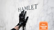 Image of a white and grey marbled surface with the name HAMLET engraved into it. A hand dripping with a dark liquid reaches t