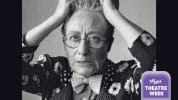 Black and white photo of Terry Baum with her hands in her hair. Terry wears round glasses and a floral polkadot suit.