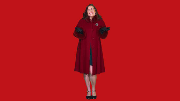 a brunette white woman in a red coat and black gloves smiles up at the sky