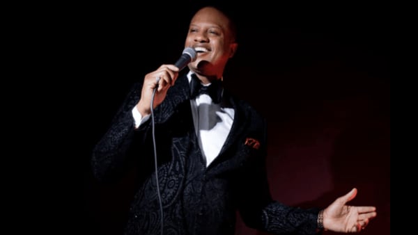 A photo of an elegantly-dressed Elijah Rock, singing into a microphone.