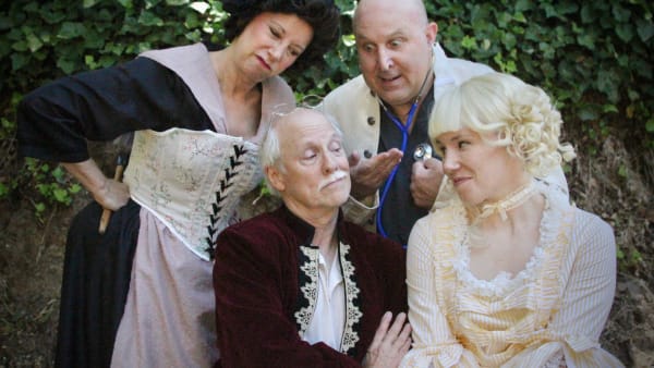 Doctor Purgeon (David Ghilardi) examines Argan (Bruce Kaplan) while Toinette (Kim Saunders) and Angelique (Skyler Wuolle) loo