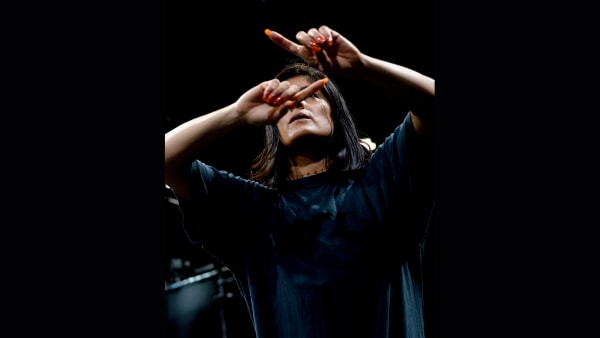 Dancer with long dark hair gestures above face with orange finger nails