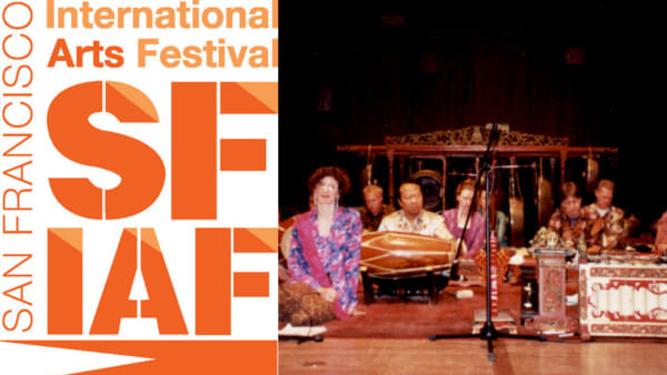 A group of Javanese musicians and vocalists sit together in the spotlight on the floor