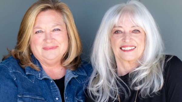 two white women one blonde and one with white hair sitting and smiling next to one another