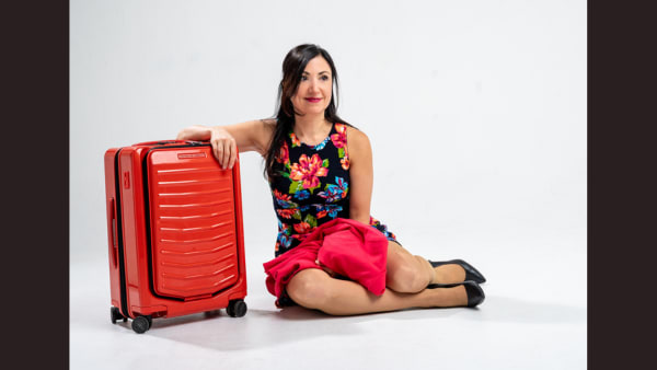 a woman in a floral dress sits on the ground next to an orange suitcase