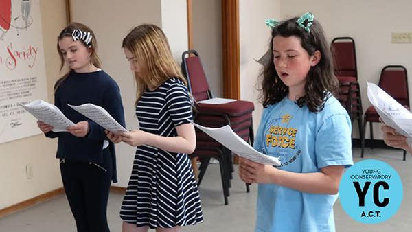 Students read lines from a script in a classroom setting.