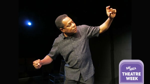 Brian Copeland with arms outstretched, wearing a gray shirt, in a blackbox theater