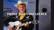 A blurry image of a man singing wearing cowboy attire: a black cowboy shirt, yellow bandana and white cowboy hat