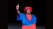 black woman in a blue shirt with red polka dotted head scarf, neck scarf, and apron