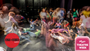 A time lapse photo of students dressed in colorful clothing all over a stage, engaged in activity and movement