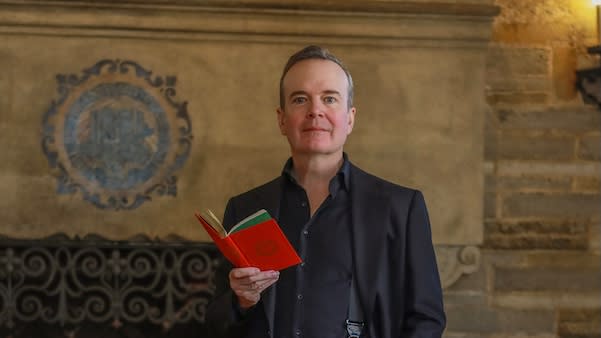 Jefferson Mays stands holding a copy of Dickens' A Christmas Carol