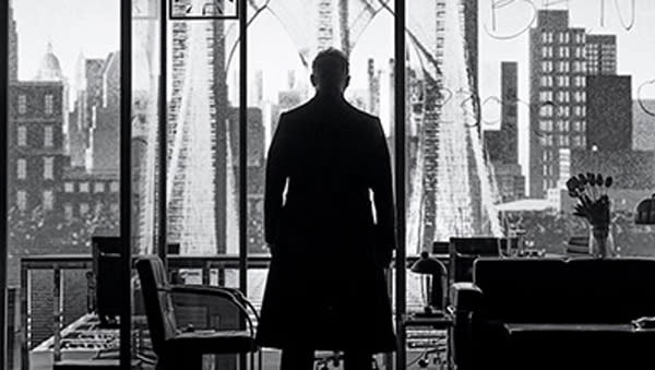 In a black and white photo, a man stands in silhouette looking out at a city skyline.