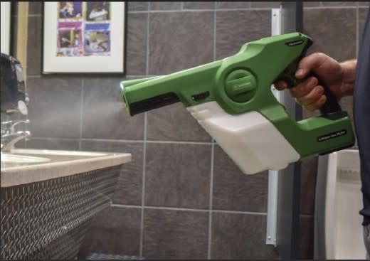 Worker using an electrostatic sprayer to disinfect restroom surfaces, ensuring a safe and sanitized environment.