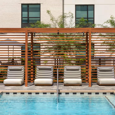 Pool cabana with comfortable lounge seating at Home2 Suites/Hampton Inn Austin East Side, surrounded by greenery and poolside