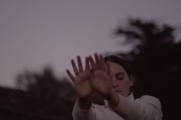 The dancer is outside, stretching their hands toward camera.