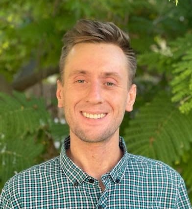 man in checkered shirt with green tree in background