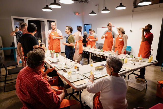 A group of people engaged in an ENAB workshop. Participants of various ages are wearing orange aprons.