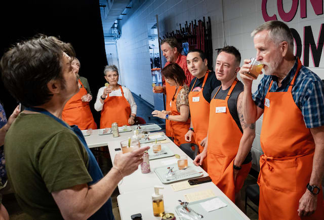 A group of people wearing orange aprons stand around a table during an ENAB Lab workshop.