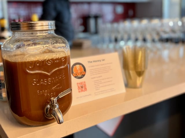 A close-up of a glass dispenser filled with an Elevated Non-Alcoholic Beverage on a white counter.