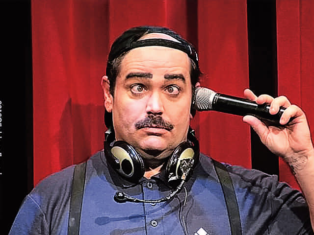 a man wearing a headset and backwards ballcap holding a microphone to his ear