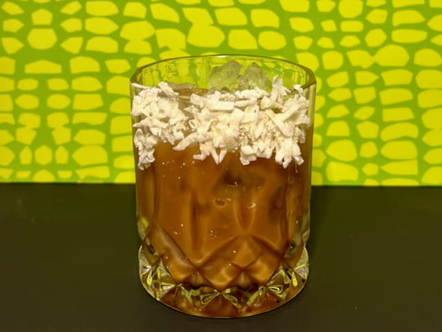 A close-up of a glass of an ENAB with a shredded coconut rim.