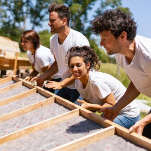 Four people work together to raise a wall of a home.
