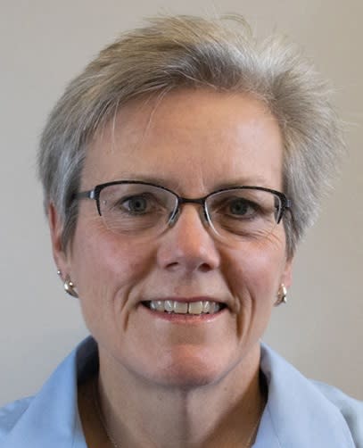 picture of Carol Horner, smiling with glasses, grey hair, dolphin earrings, wearing a blue blouse