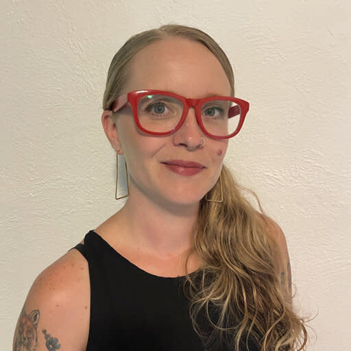 Female with long blonde hair, red-rimmed glasses, and a black sleeveless shirt