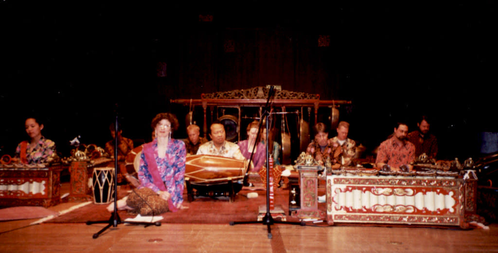 A group of Javanese musicians and vocalists sit together in the spotlight on the floor