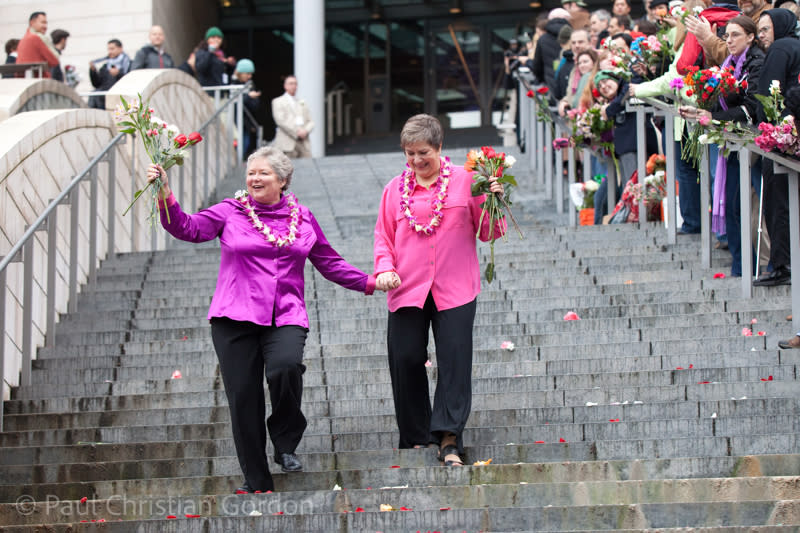 A newly married couple is handed flowers by supporters as they leave City Hall.