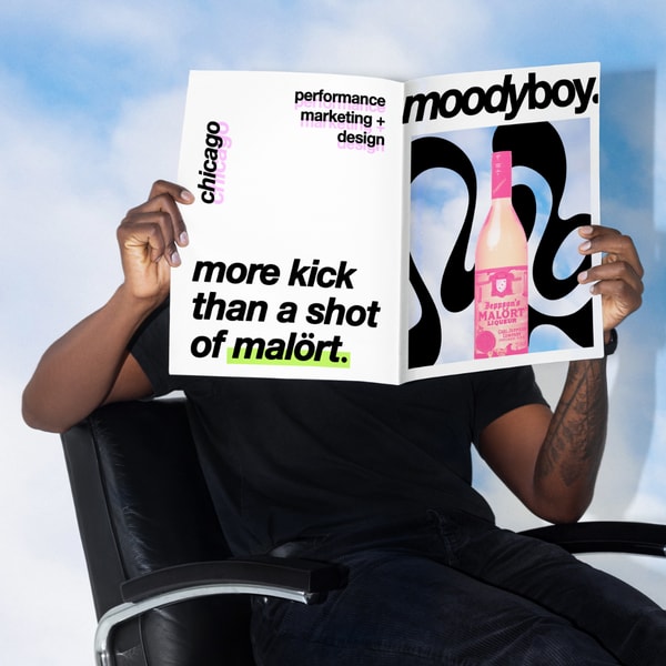 Person holding a Moodyboy Marketing Studio magazine spread with bold typography and Malört-inspired creative.