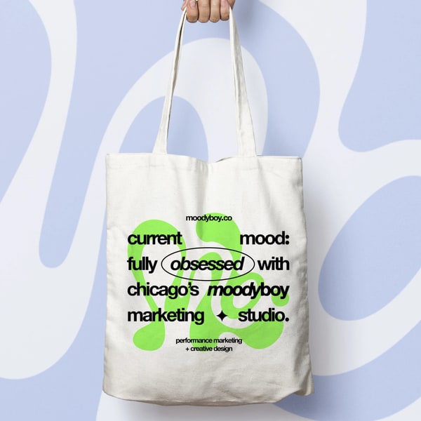 Tote bag with Moodyboy Marketing Studio branding in bold green and black typography.