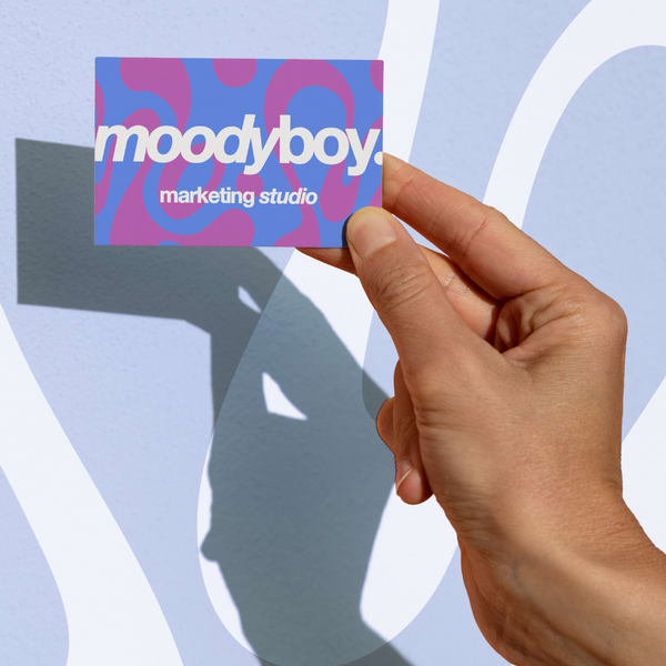 Person holding a Moodyboy Marketing Studio business card with bright pink and blue abstract patterns.