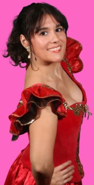 a dancer in a red dress with short sleeves smiles at the camera with hands on hips