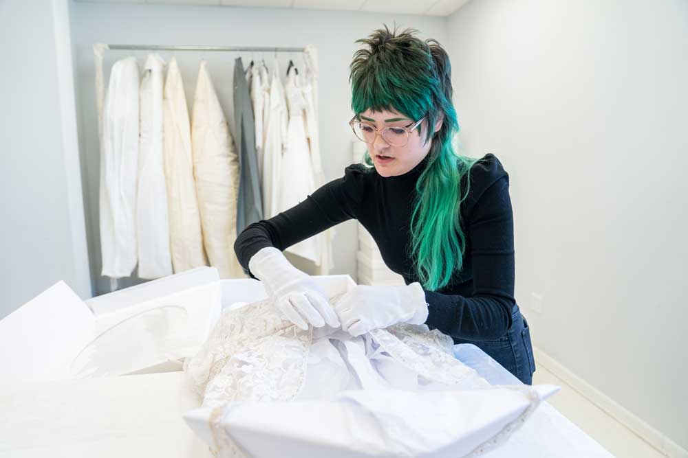 Carefully packaging a wedding gown with acid-free tissue and into an acid-free heirloom preservation chest