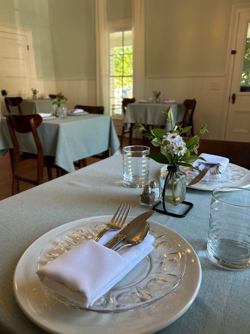 Table set with plates, napkins, silverware and glasses. White flowers in center vase.