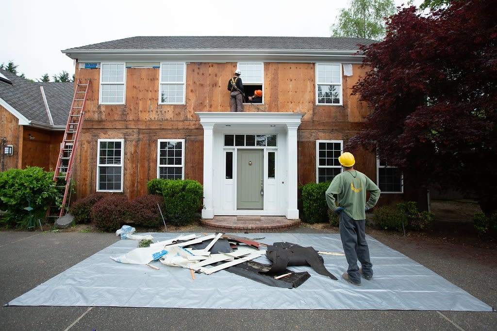 Photo of home with siding removed, a team of workers with materials spread out on the ground