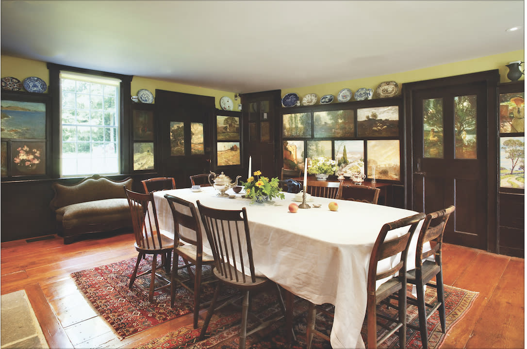 A historic dining room with painted wall panels, long dining table surrounded by chairs, candlesticks and decor on the table