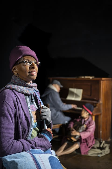 Velina Brown in winter clothes in front of actors sitting around a piano and out of focus
