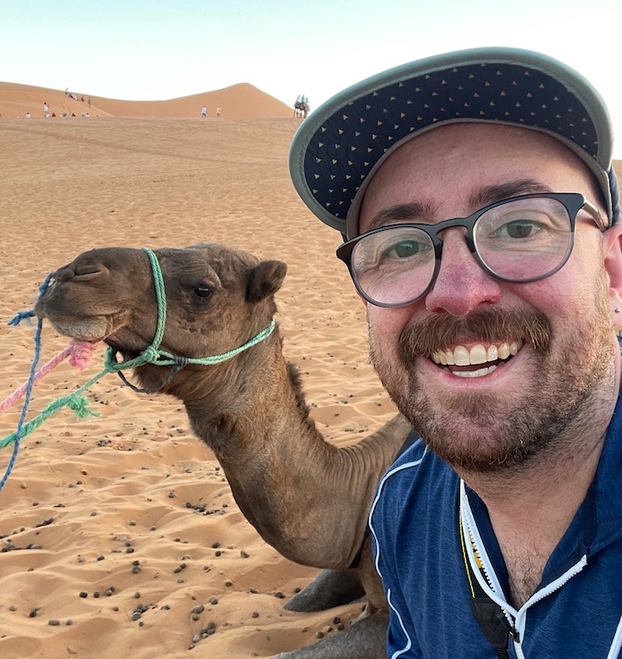 photo of Travel Advisor/Proprietor Michael Cole-Schwartz in the desert with a camel in the background