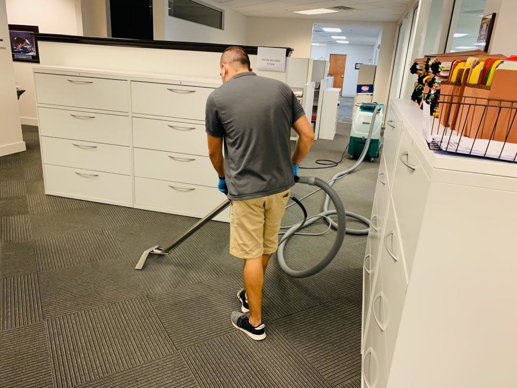 Janitorial worker using professional hot water extraction equipment to deep clean office carpet flooring, ensuring a fresh an
