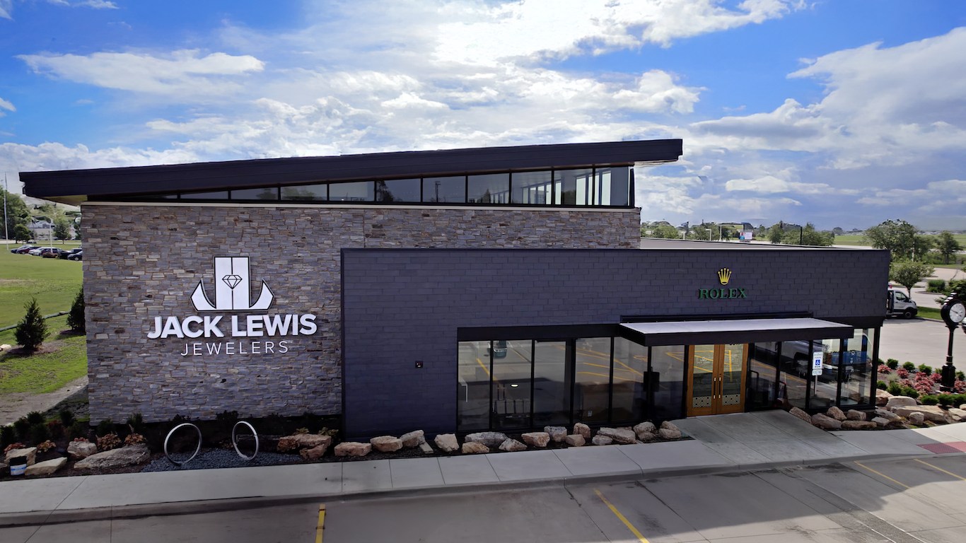 Exterior view of Jack Lewis Jewelers building with prominent signage and Rolex storefront under a partly cloudy sky.