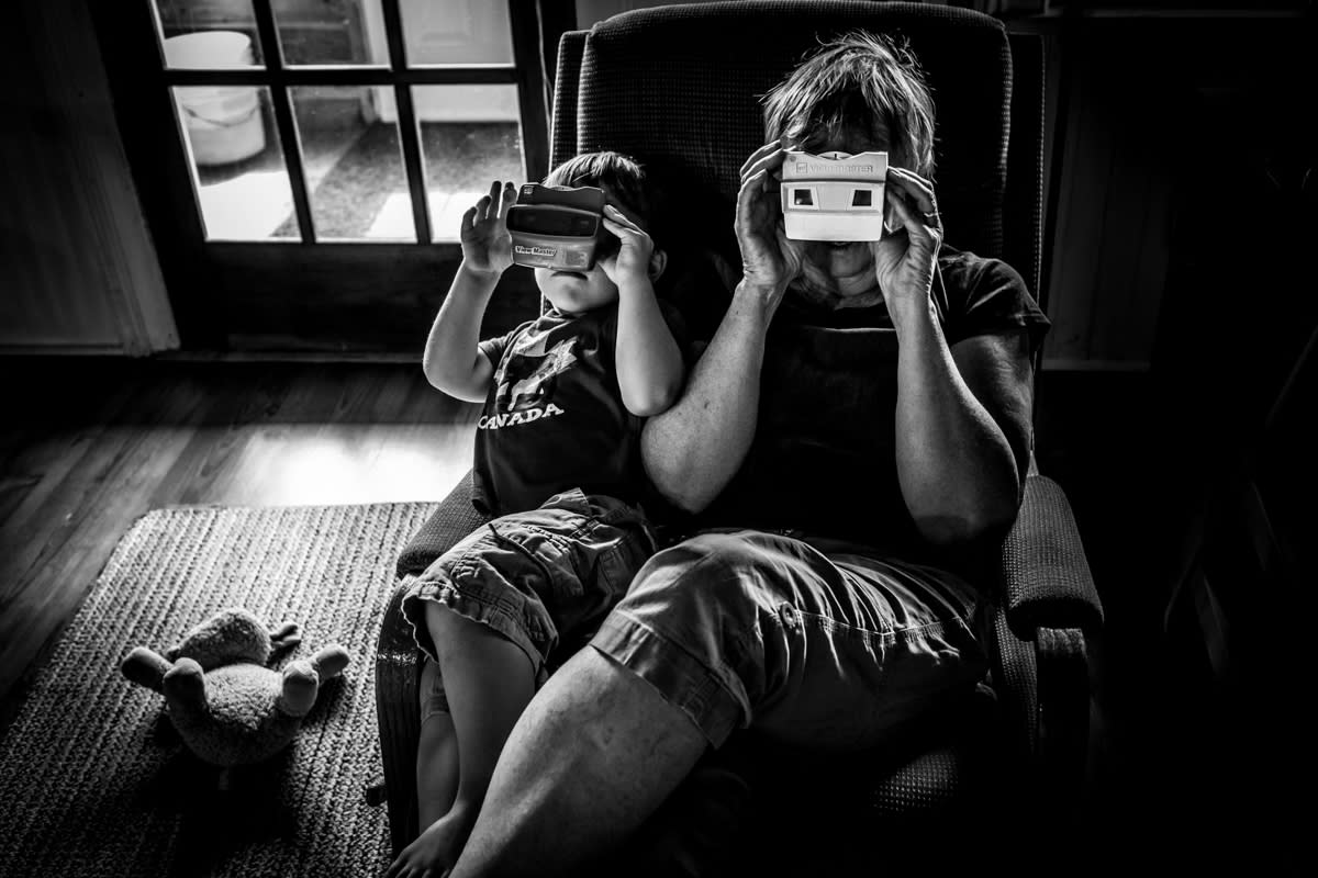documentary photograph of Grandma and grandson sitting side by side looking through Viewmasters while toy sheep is discarded